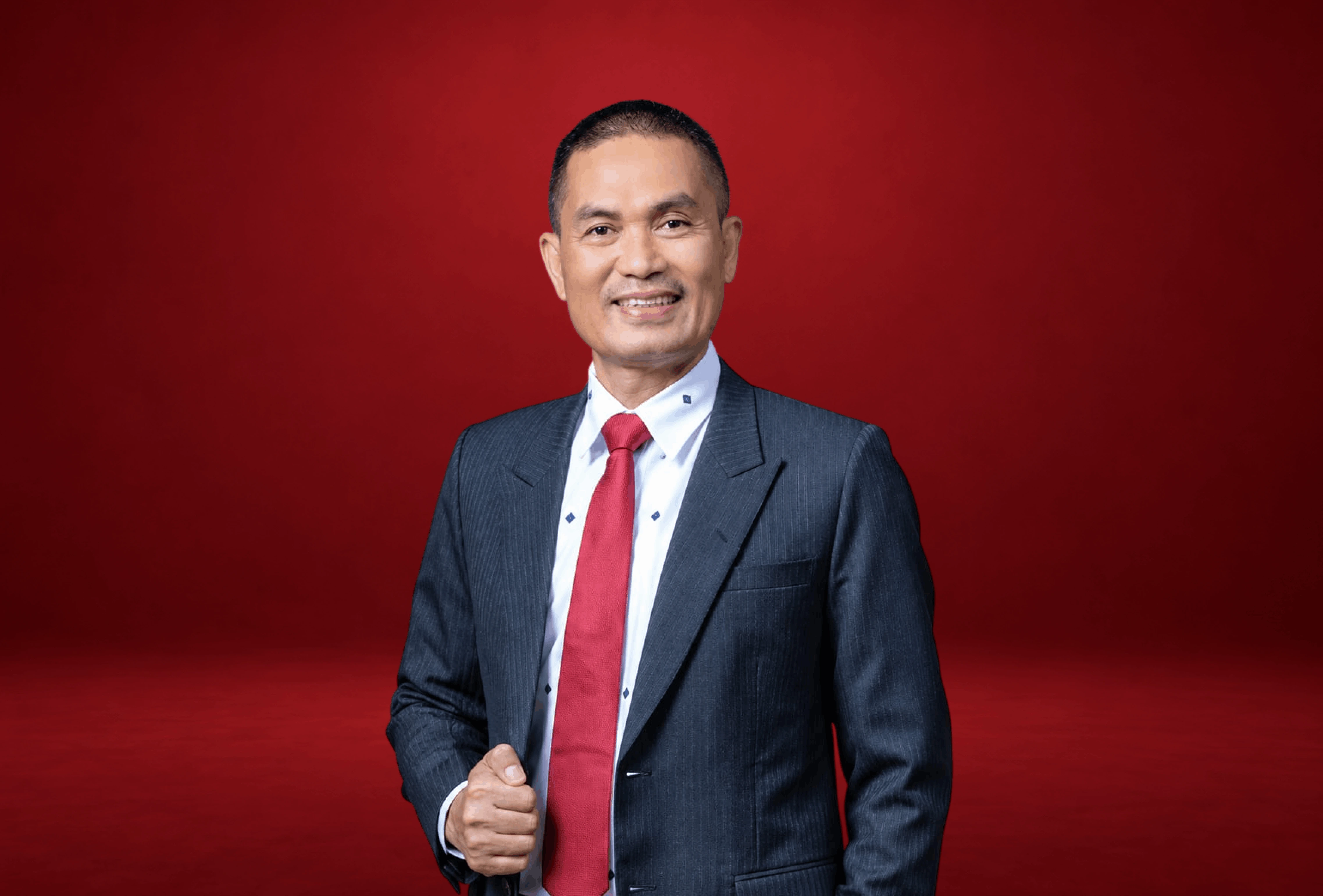 Dr. Sopian Sitepu in a studio portrait, wearing a dark suit and tie, standing with a calm and confident expression in a polished corporate setting